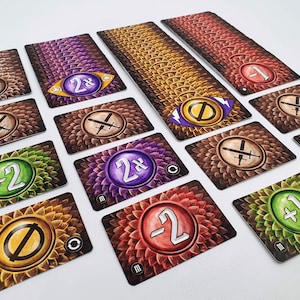 May include: A set of game cards with different symbols and numbers. The cards have a brown, green, purple, or orange background with a circular design. The symbols include swords, a zero, and a 2x multiplier. The numbers include +0, +1, +2, -1, and -2.