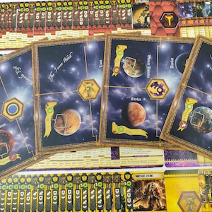 May include: Board game components featuring space-themed artwork. The cards display planets, constellations, and text such as "The Inner Watch" and "The Galactic Core." The color palette includes blues, browns, and golds, with various game pieces visible.