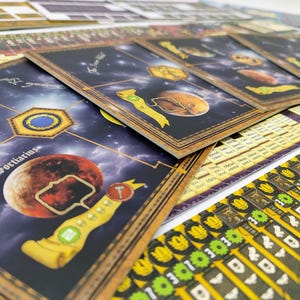 May include: A collection of board game cards featuring a space theme. The cards display planets, constellations, and other celestial elements against a dark blue background. The cards have a wooden border and are accompanied by game tokens.