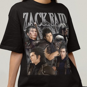 Może przedstawiać: Czarny t-shirt z srebrną grafiką Zacka Fair i napisem "ZACK FAIR". Projekt zawiera kilka portretów postaci. Koszulka jest z krótkim rękawem i ma okrągły dekolt.