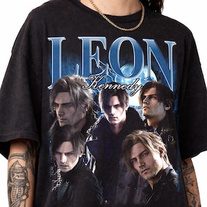 May include: Black t-shirt featuring a graphic of Leon Kennedy from the video game Resident Evil. The design includes the name "LEON Kennedy" in blue and white, with multiple images of the character. The shirt has a vintage, worn look.