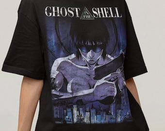 May include: Black t-shirt featuring a graphic from the anime series Ghost in the Shell. The design includes a character holding a gun, with the text "GHOST SHELL" above. The shirt is worn with gray shorts.