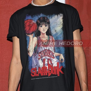 Può includere: Maglietta nera con una stampa grafica di una giocatrice di basket che tiene una palla. La grafica è in stile vintage con un effetto invecchiato. Il testo "Slam Dunk" è stampato sotto la grafica.