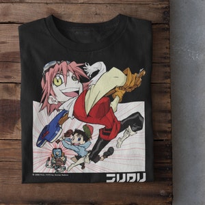Puede incluir: Camiseta negra con un gráfico blanco de un personaje de dibujos animados con cabello rosado y un atuendo rojo y amarillo. El personaje sostiene un arma azul y blanca. El texto "FLCL" y "フリクリ" está impreso en la camiseta.