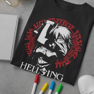 Puede incluir: Camiseta negra con un gráfico blanco de un personaje sosteniendo un arma. El gráfico está rodeado de un círculo rojo con el texto "Hellsing" y una serie de símbolos en rojo.