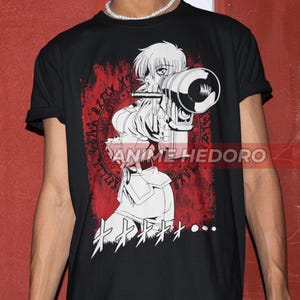 Könnte beinhalten: Schwarzes T-Shirt mit einer weißen Anime-Figur, die eine Waffe hält. Die Figur ist von einem roten Kreis mit weißem Text umgeben. Der Text auf dem T-Shirt lautet "キササ..."