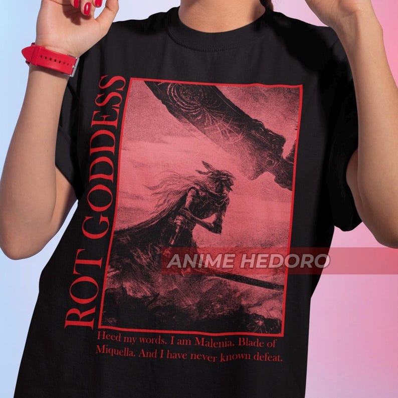 May include: Black t-shirt with a red graphic print of a character from the video game Elden Ring. The graphic includes the text "ROT GODDESS" and "ANIME HEDORO". The text below the graphic reads "Heed my words. I am Malenia. Blade of Miquella. And I have never known defeat."