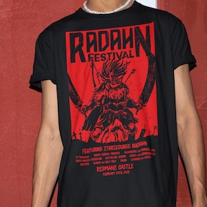 May include: Black t-shirt with a red graphic print of a warrior holding two swords. The graphic includes the text "Radahn Festival" and "Featuring Starscourge Radahn". The text also includes the names of various characters and the date "February 25th, 2022".