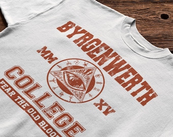 May include: A white t-shirt featuring a distressed rust-colored graphic. The design includes the text BYRGENWERTH COLLEGE, the Roman numerals MM and XV, and a central circular emblem containing a triangle with an eye and various symbols.