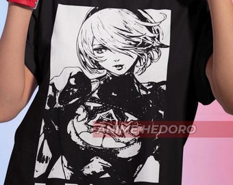 May include: Black and white graphic t-shirt featuring a stylized illustration of a female character with short hair. The text "ニーア オートマタ" is printed below the image.