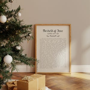 Può includere: Una stampa incorniciata con il testo "The birth of Jesus" e la Scrittura di Luca 2:7-18. La stampa è in una cornice di legno chiaro ed è esposta su un pavimento di legno. Un albero di Natale con ornamenti e regali confezionati sono in primo piano.