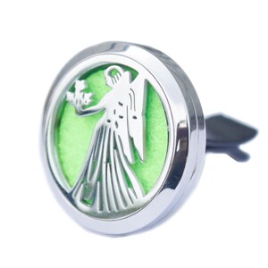 May include: A silver car air vent diffuser with a circular design. The design features a white Virgo figure on a light green background. The diffuser has a black clip for attachment.