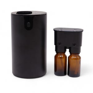 May include: A black essential oil diffuser with a cylindrical base and a separate black component holding two amber glass bottles. The diffuser has a sleek, modern design, perfect for aromatherapy.