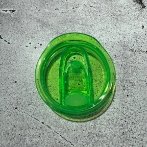 May include: A green plastic lid for a travel mug with a sliding closure.