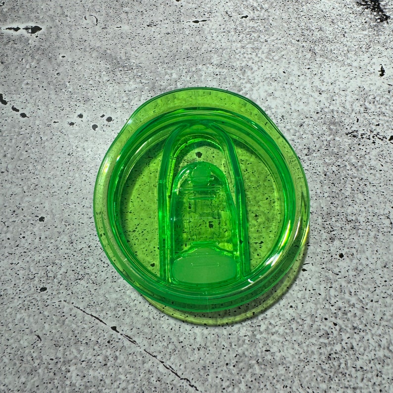 May include: A green plastic lid for a travel mug with a sliding closure.