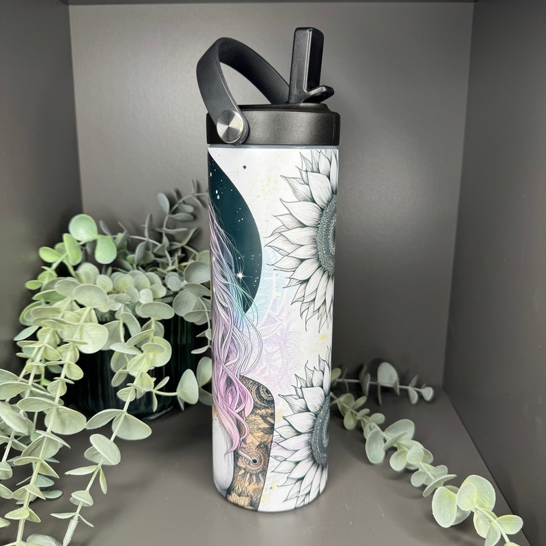 May include: A white stainless steel tumbler with a black lid and a black handle. The tumbler has a design of a woman with long hair and sunflowers.