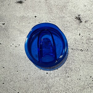 May include: A blue plastic lid for a travel mug with a blue plastic slider.