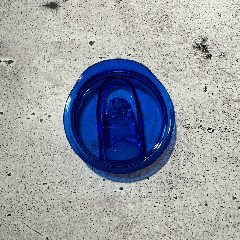 May include: A blue plastic lid for a travel mug with a blue plastic slider.