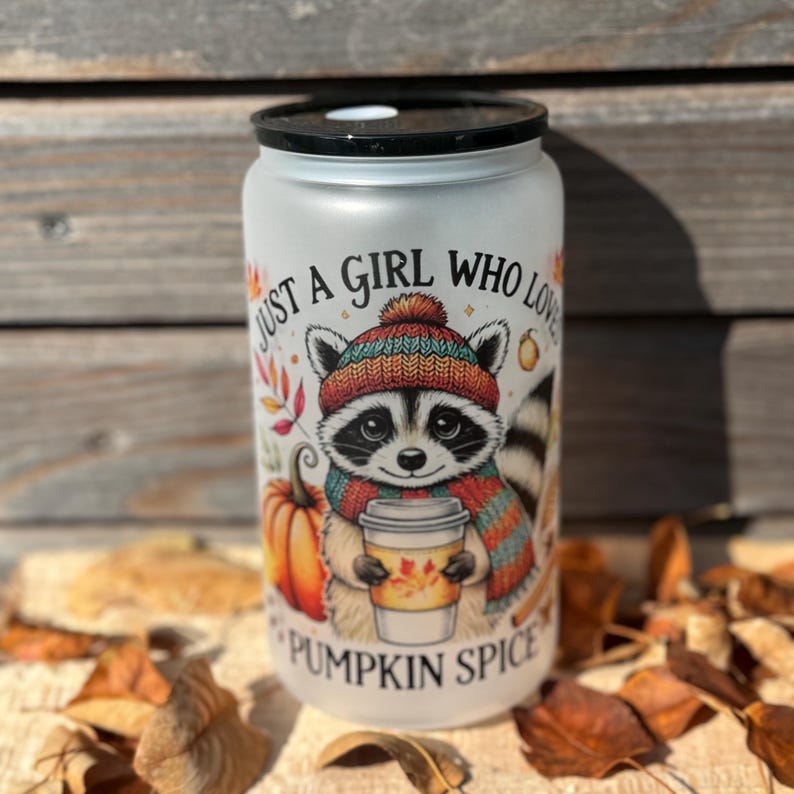 Op de afbeelding: Een witte tumbler met een wasbeer die een hoed en sjaal draagt en een kopje koffie vasthoudt. De tumbler is versierd met de tekst "Just a girl who loves pumpkin spice".