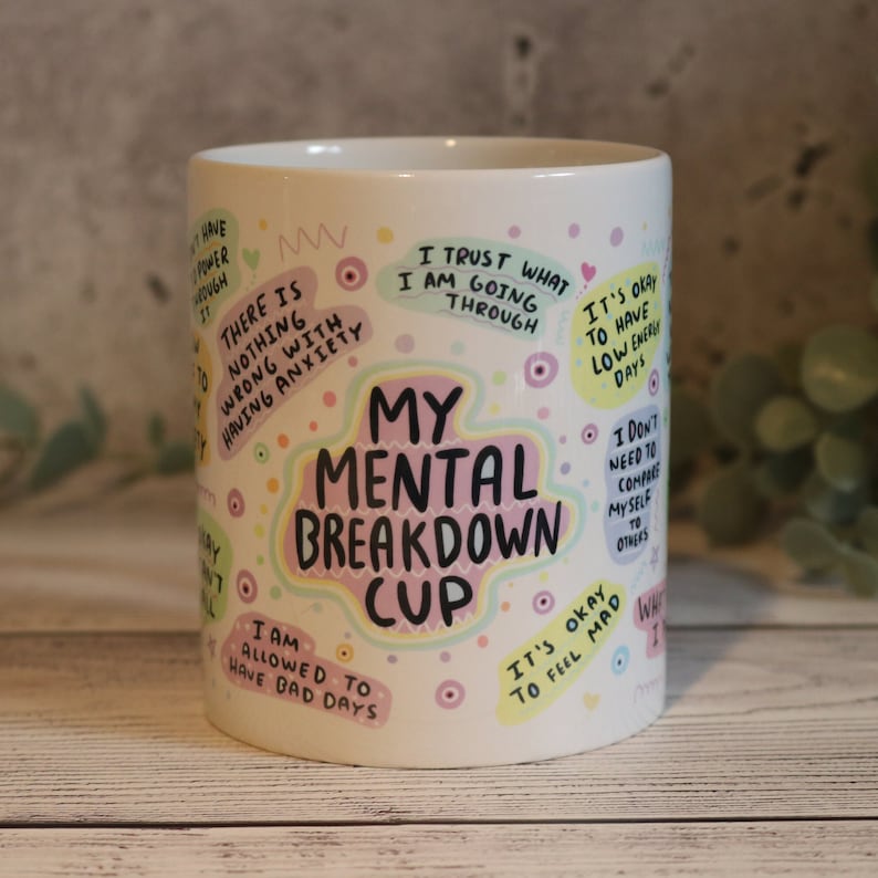 Pu&ograve; includere: Una tazza in ceramica bianca con un design colorato che presenta il testo "My Mental Breakdown Cup" e varie affermazioni positive. Le affermazioni includono "Mi fido di quello che sto attraversando", "Non c'&egrave; niente di sbagliato nell'avere ansia", "Mi &egrave; permesso avere giornate brutte", "Va bene avere giornate con poca energia", "Va bene sentirsi arrabbiati", e "Non ho bisogno di confrontarmi con gli altri".