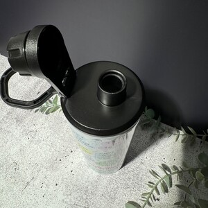 May include: A black and white water bottle with a black lid and a carrying handle. The bottle has a variety of colorful words and phrases printed on it.