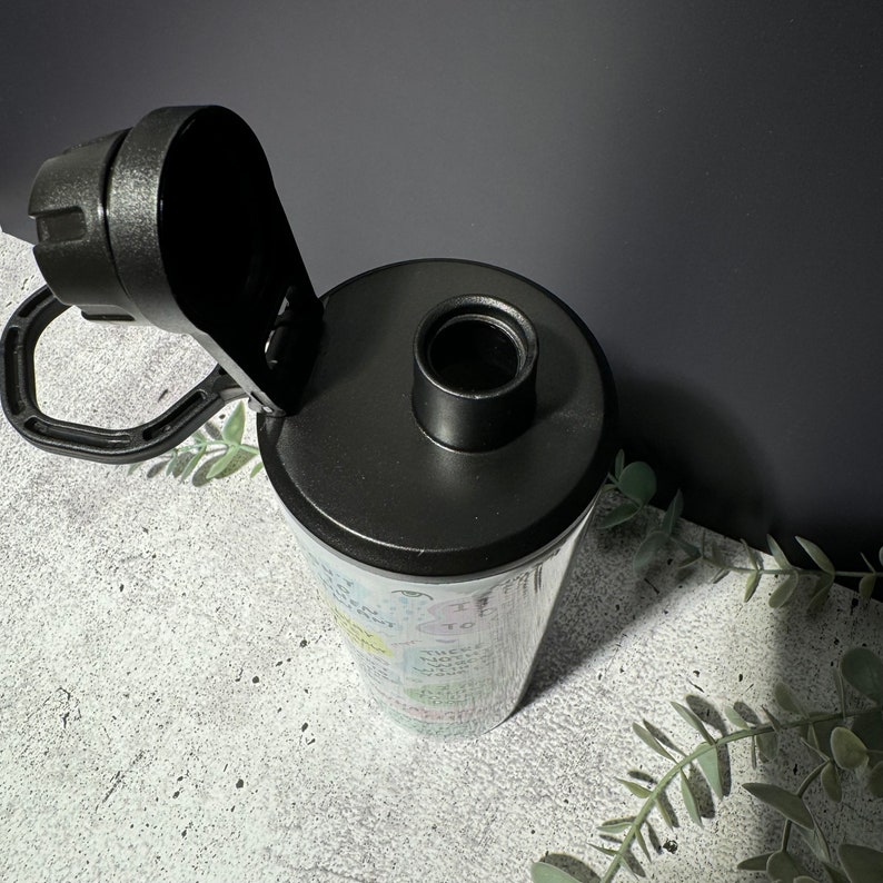 May include: A black and white water bottle with a black lid and a carrying handle. The bottle has a variety of colorful words and phrases printed on it.