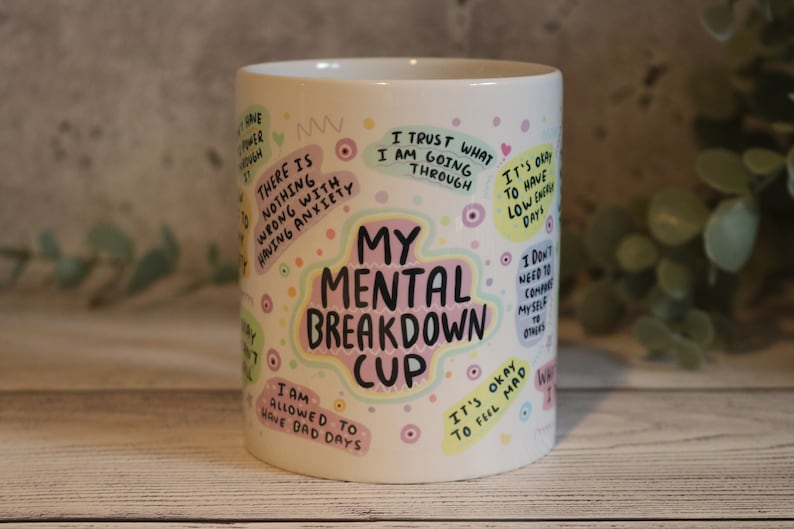 Pu&ograve; includere: Tazza in ceramica bianca con testo e illustrazioni colorate. Il testo recita "My Mental Breakdown Cup" e include frasi come "Mi &egrave; permesso avere giornate brutte" e "Va bene sentirsi arrabbiati".