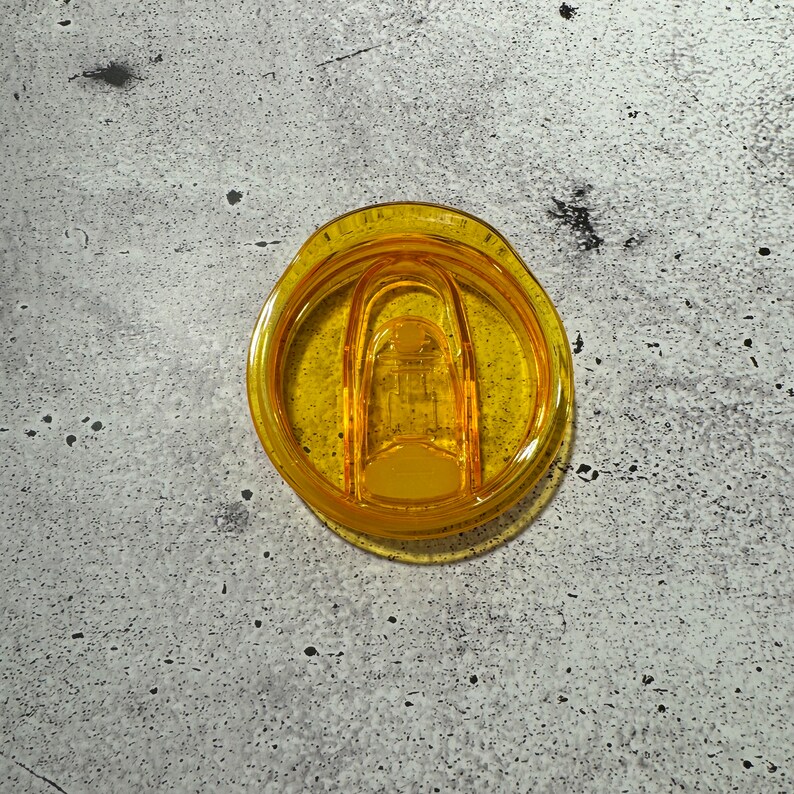 May include: A yellow plastic lid for a travel mug with a clear plastic slider.