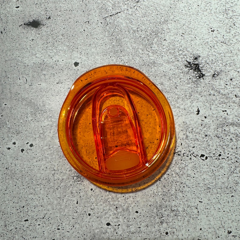 May include: Orange plastic lid for a travel mug with a clear plastic lid insert.