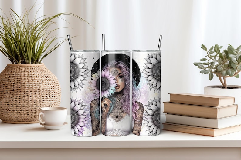 May include: Three stainless steel tumblers with a white background and a design of a woman with a sunflower behind her. The woman has pink hair and tattoos. The sunflowers are black and white with a rainbow colored center.