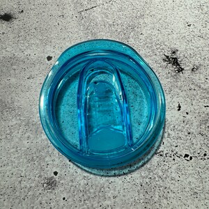 May include: A light blue plastic lid for a travel mug with a sliding closure.