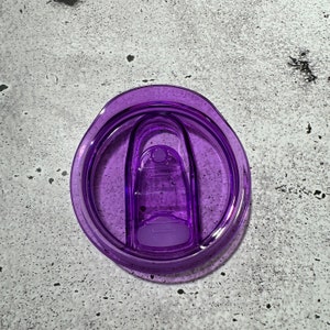 May include: Purple plastic lid for a travel mug with a sliding closure.