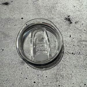 May include: A clear plastic lid for a travel mug with a silicone seal and a locking mechanism.