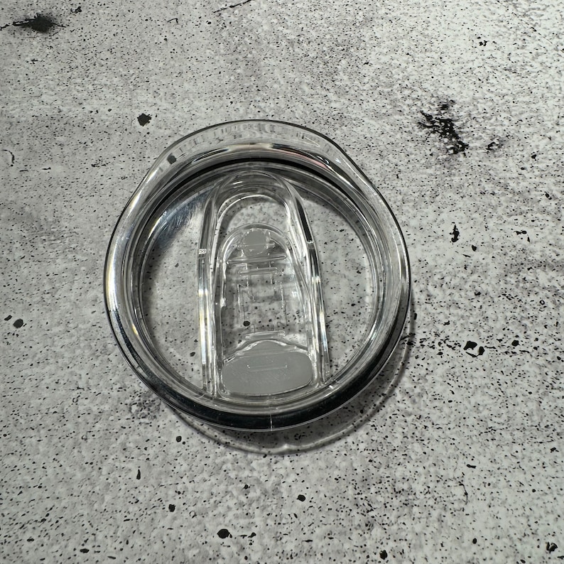 May include: A clear plastic lid for a travel mug with a silicone seal and a locking mechanism.