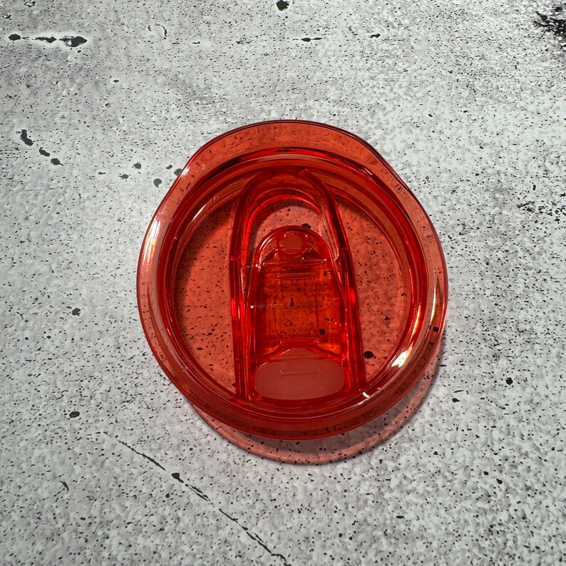 May include: A close-up of a bright orange plastic lid for a travel mug. The lid has a silicone seal and a flip-top lid.