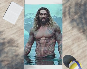 Può includere: Un uomo con i capelli lunghi castani e la barba è in piedi nell'acqua. Indossa un costume da bagno nero e ha dei tatuaggi sul petto e sulle braccia. Lo sfondo è un cielo blu con nuvole bianche.