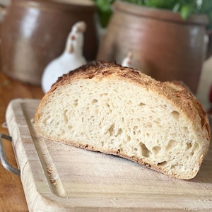 May include: A close-up of a freshly baked loaf of bread sliced in half, revealing a soft, airy crumb. The bread is on a wooden cutting board.