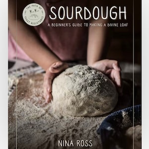 May include: A book cover with the title "SOURDOUGH: A Beginner's Guide to Making a Divine Loaf" by Nina Ross. The cover features a close-up of a hand shaping a loaf of sourdough bread.