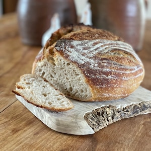 May include: A freshly baked loaf of sourdough bread with a crispy crust and a soft, airy crumb. The bread is sliced and placed on a rustic wooden cutting board.