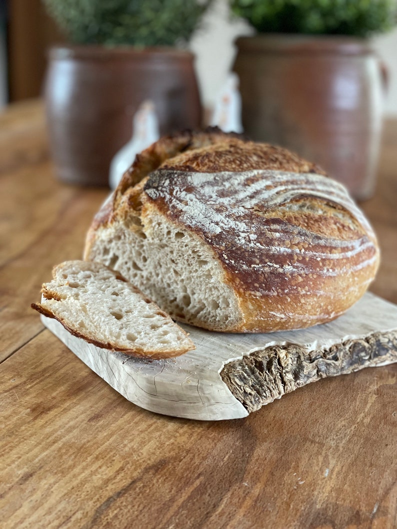May include: A freshly baked loaf of sourdough bread with a crispy crust and a soft, airy crumb. The bread is sliced and placed on a rustic wooden cutting board.