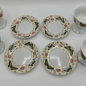 Peut inclure: Ensemble de quatre soucoupes en porcelaine blanche avec des bordures dor&eacute;es et des motifs de papillons. Chaque soucoupe a un puits central pour une tasse. Les soucoupes sont accompagn&eacute;es de deux tasses assorties avec des bordures dor&eacute;es et des motifs de papillons.