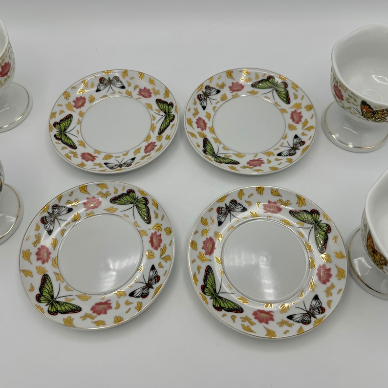 Peut inclure: Ensemble de quatre soucoupes en porcelaine blanche avec des bordures dor&eacute;es et des motifs de papillons. Chaque soucoupe a un puits central pour une tasse. Les soucoupes sont accompagn&eacute;es de deux tasses assorties avec des bordures dor&eacute;es et des motifs de papillons.