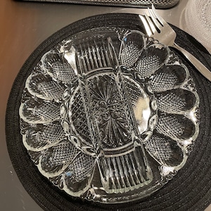 May include: A clear glass serving dish with a scalloped edge and a divided center. The dish is designed for serving individual portions of food, such as appetizers or desserts.