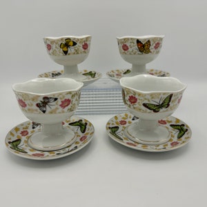 Peut inclure: Ensemble de quatre coupes &agrave; dessert en porcelaine blanche avec soucoupes assorties. Chaque coupe et soucoupe pr&eacute;sente un motif floral avec des papillons dans des tons de vert, jaune, orange et marron.