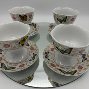 Peut inclure: Ensemble de quatre coupes &agrave; dessert en porcelaine blanche avec des bordures dor&eacute;es et des motifs de papillons. Chaque coupe est accompagn&eacute;e d'une soucoupe assortie avec un motif floral.