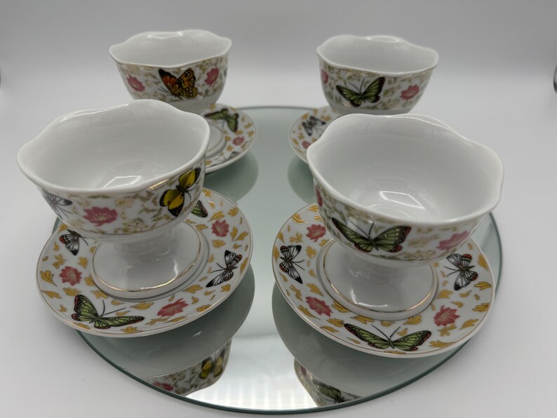 Peut inclure: Ensemble de quatre coupes &agrave; dessert en porcelaine blanche avec des bordures dor&eacute;es et des motifs de papillons. Chaque coupe est accompagn&eacute;e d'une soucoupe assortie avec un motif floral.