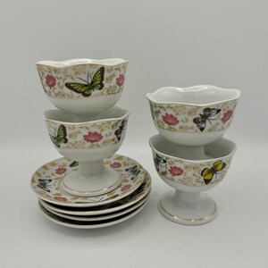 Peut inclure: Ensemble de quatre coupes &agrave; dessert en porcelaine blanche avec un pied et un motif de papillon et de fleurs. Les coupes sont empil&eacute;es par deux et se trouvent sur une surface blanche.