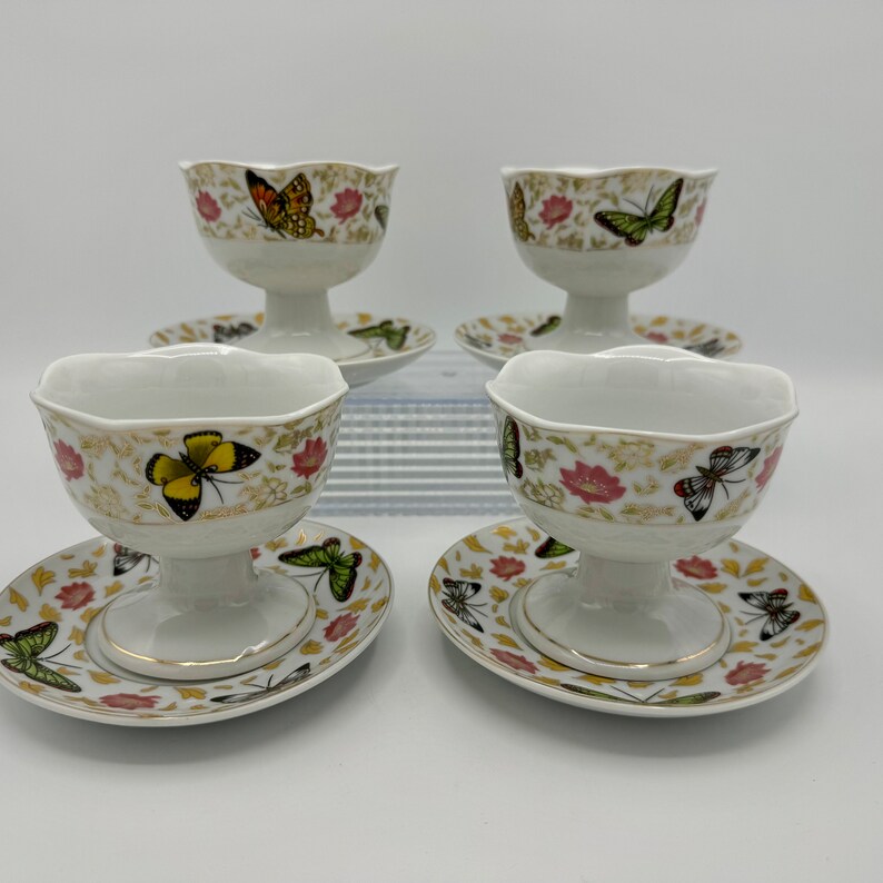 Peut inclure: Ensemble de quatre coupes &agrave; dessert en porcelaine blanche avec soucoupes assorties. Chaque coupe et soucoupe est orn&eacute;e d'un bord dor&eacute; et d'un motif floral d&eacute;licat avec des papillons color&eacute;s.