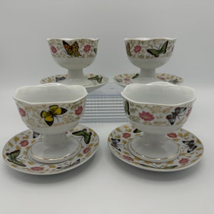 Peut inclure: Ensemble de quatre bols &agrave; dessert en porcelaine blanche avec soucoupes assorties. Chaque bol et soucoupe pr&eacute;sente un motif floral avec des papillons dans des tons de jaune, vert, orange et marron.