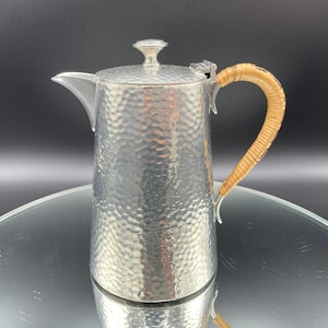 Peut inclure: Une cafetière en métal martelé argenté avec une poignée en osier brun.